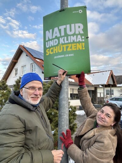 Zwei Mitglieder der Münstereifler Grünen hängen ein Wahlplakat auf.